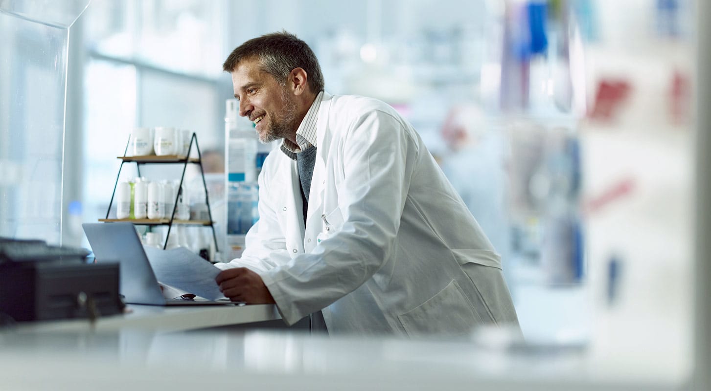 A man in a lab coat is focused on working on a laptop in a laboratory setting.